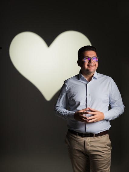 Dr. Samuel Ferro usando roupa social na frente de uma parede com um coração desehado atrás